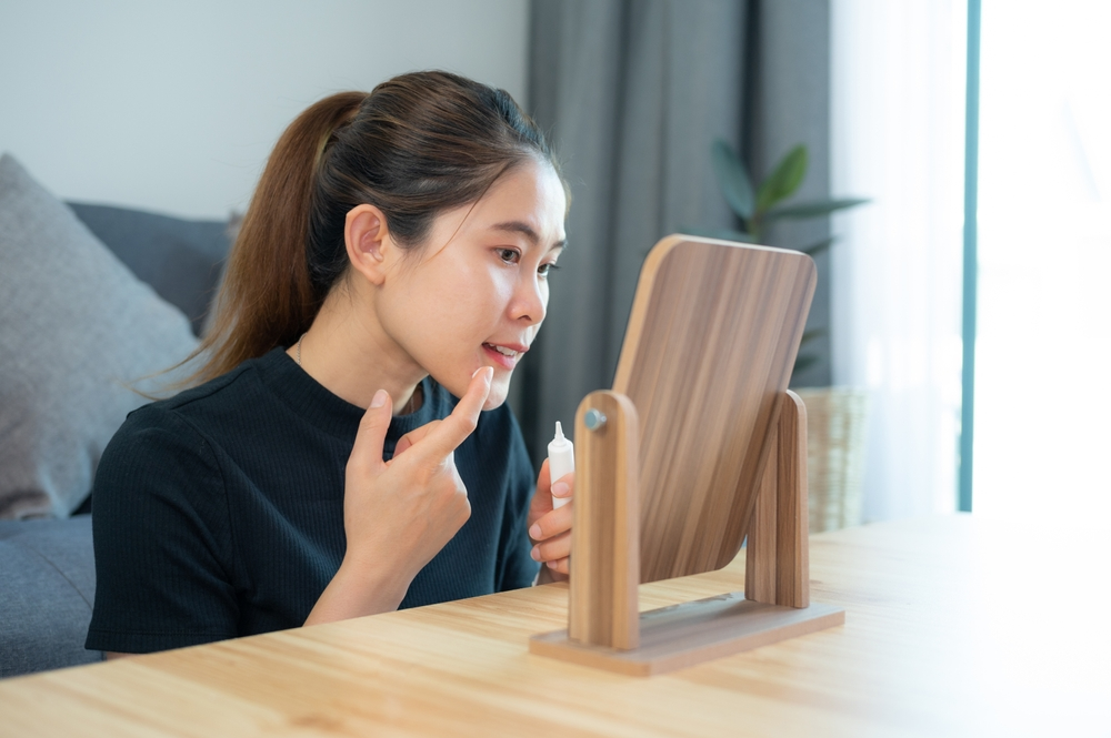 young woman applying retinoid to her face using a mirror