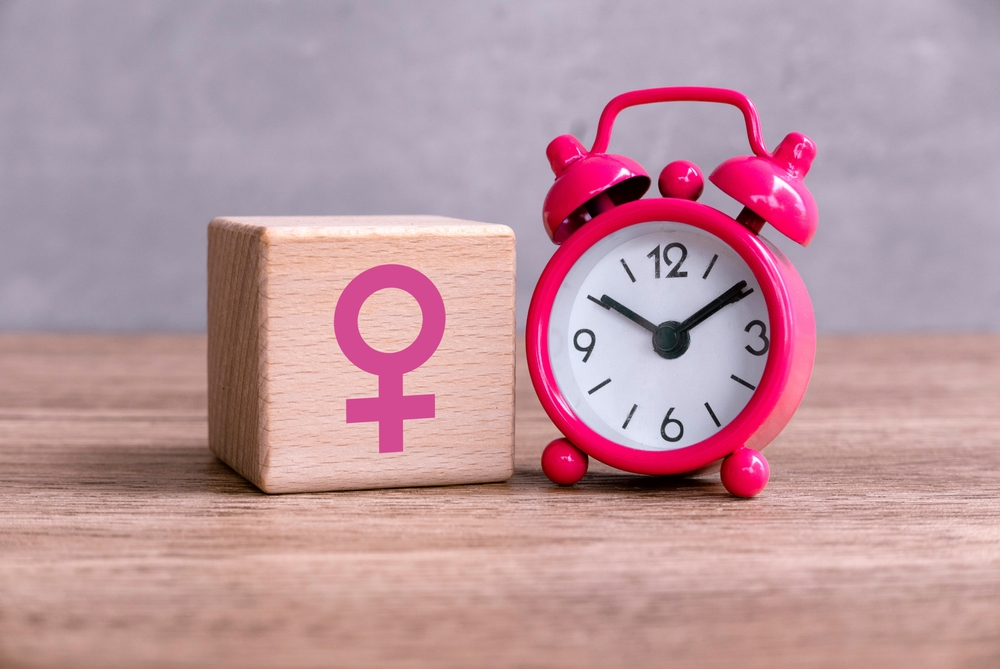 wooden block with pink female gender symbol next to pink alarm clock to represent menopause