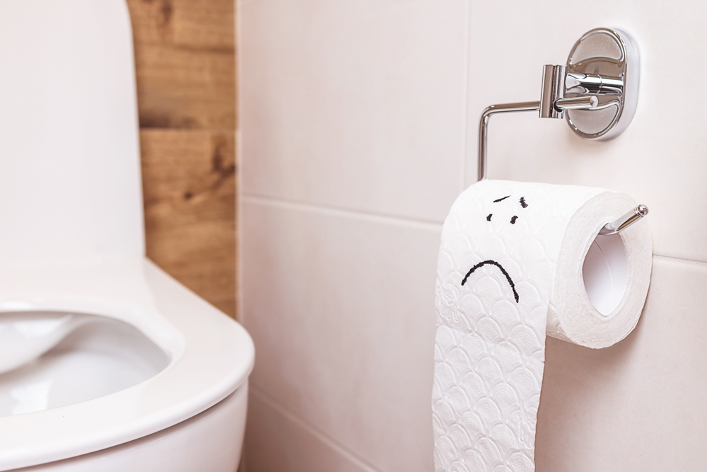 roll of toilet with sad face drawn on it next to toilet